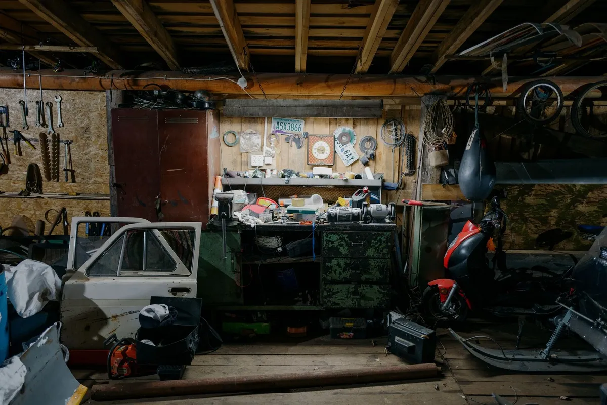 A cluttered garage filled with tools, motorcycle parts, and car door pieces, highlighting DIY junk removal challenges.